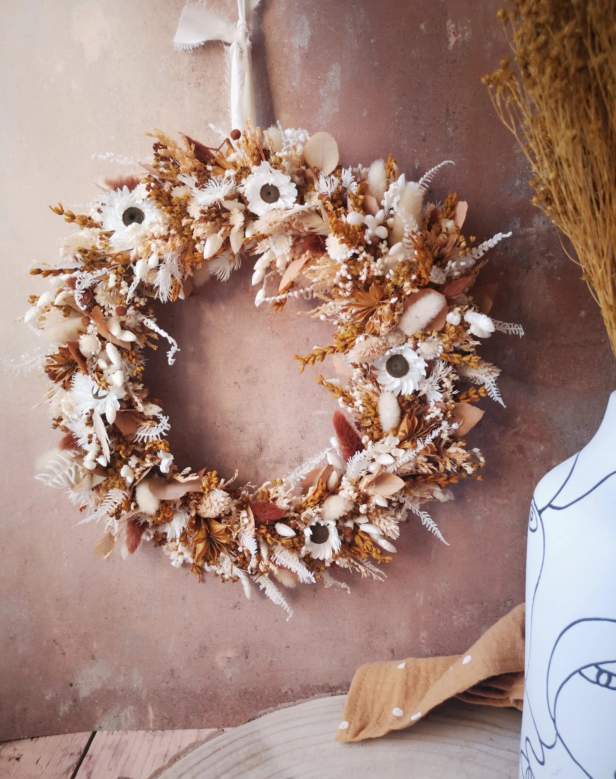 Couronne murale de fleurs séchées dans les tons blanc, terracotta et moutarde.